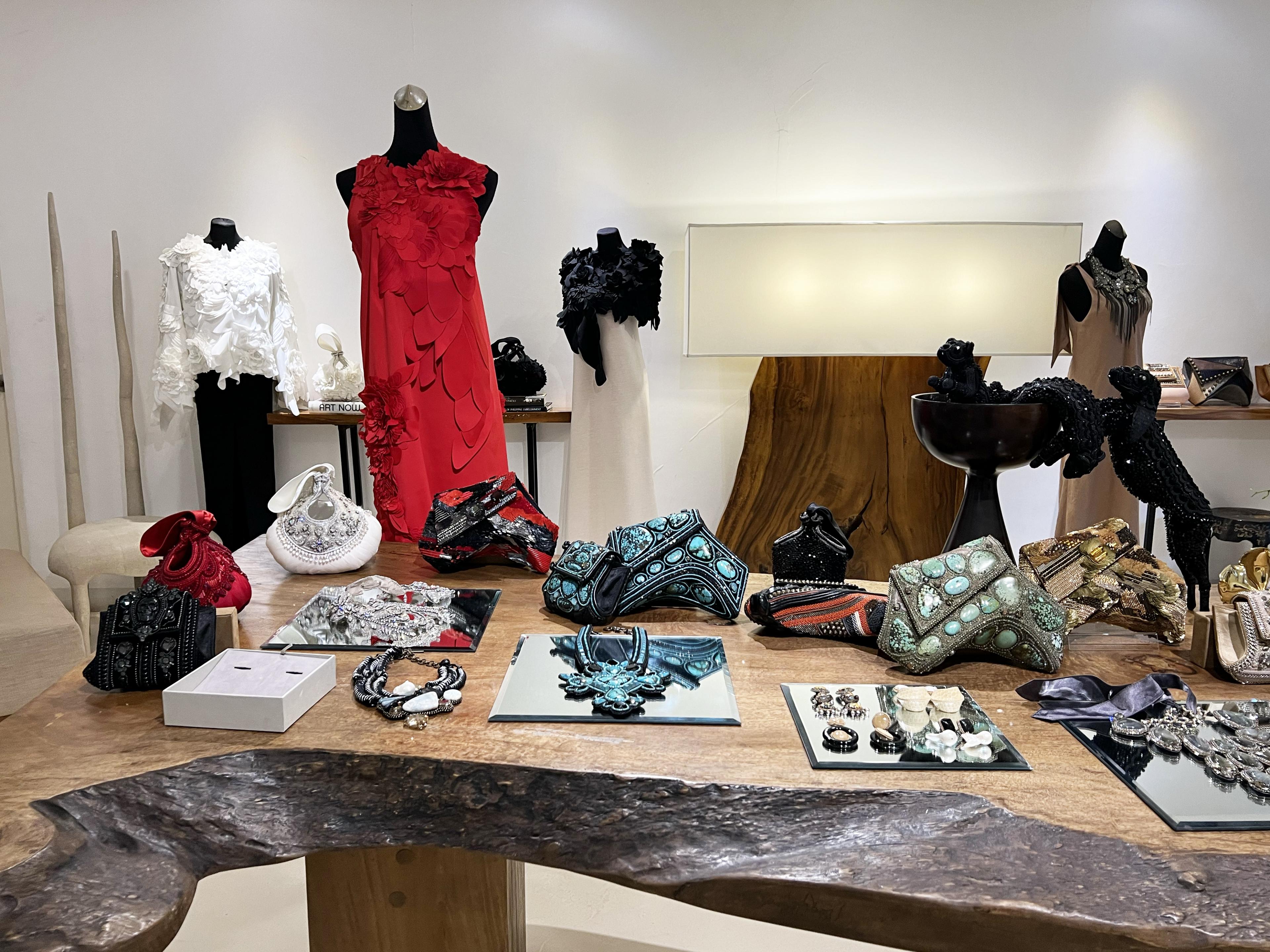 women's fashions and jewelry on display in white-walled shop with a red dress with sculptural collar