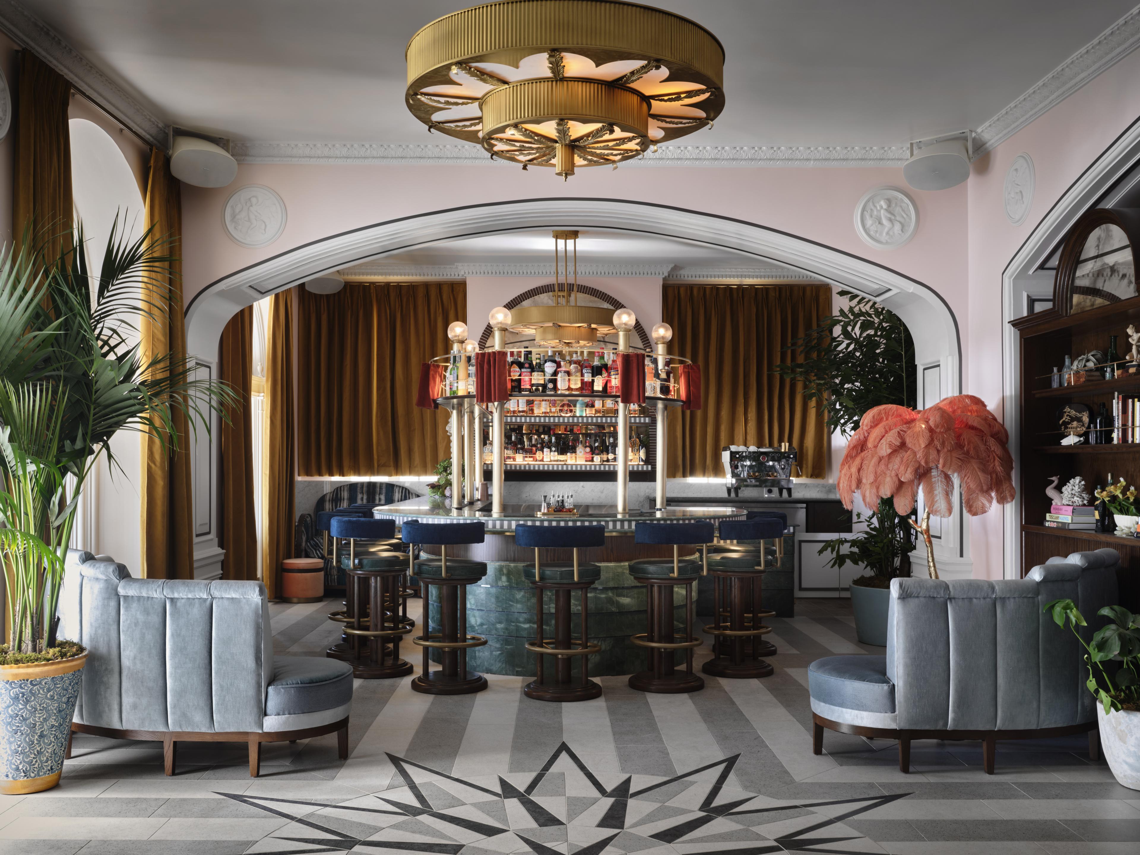 hotel bar with grand Art Deco decor and curvy banquette seating and pink walls 