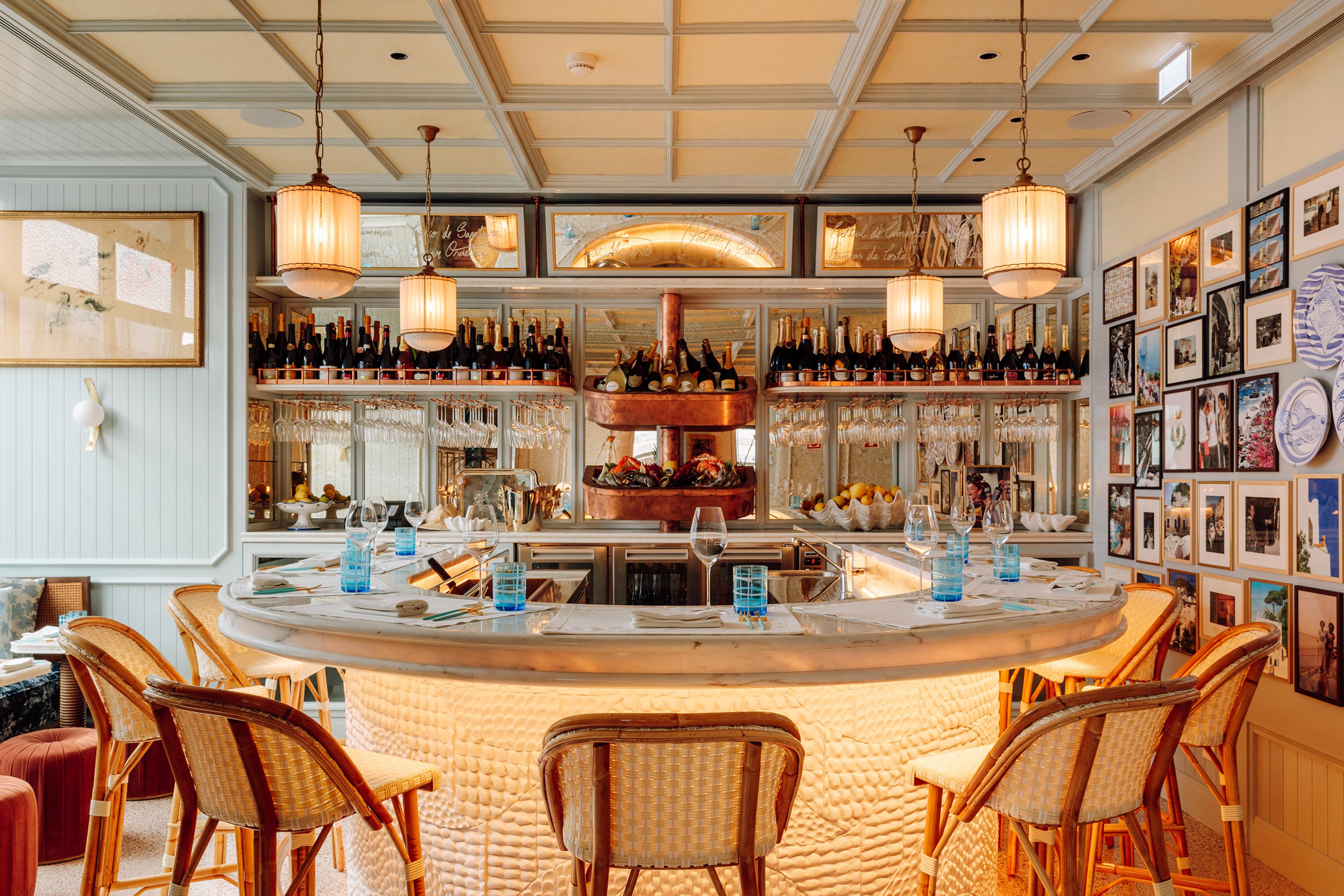 U-shaped bar surrounded by wicker chairs against a back mirrored wall stocked with champagne bottles and wine glasses