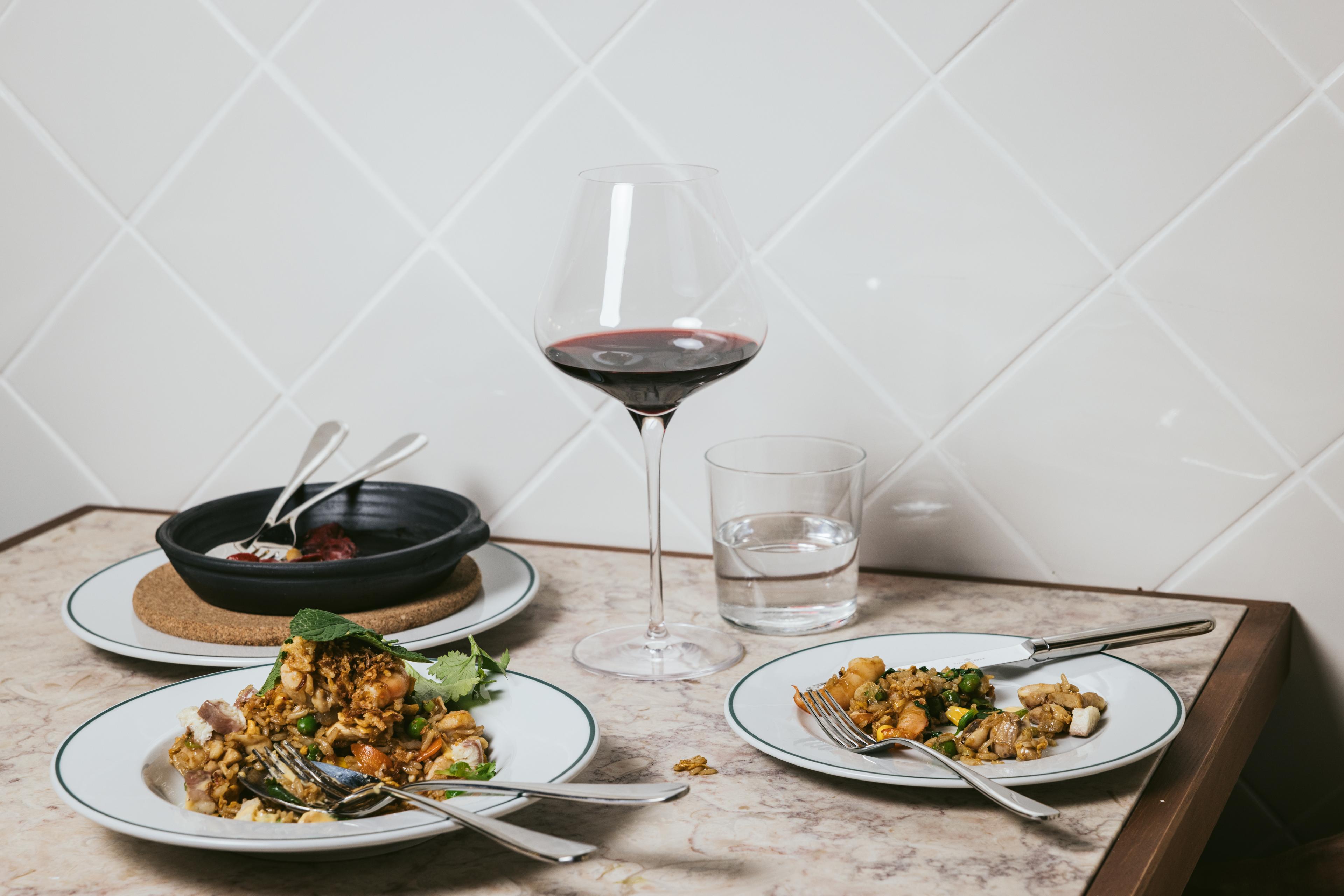 Plates of food on a tabletop with a glass of red wine 