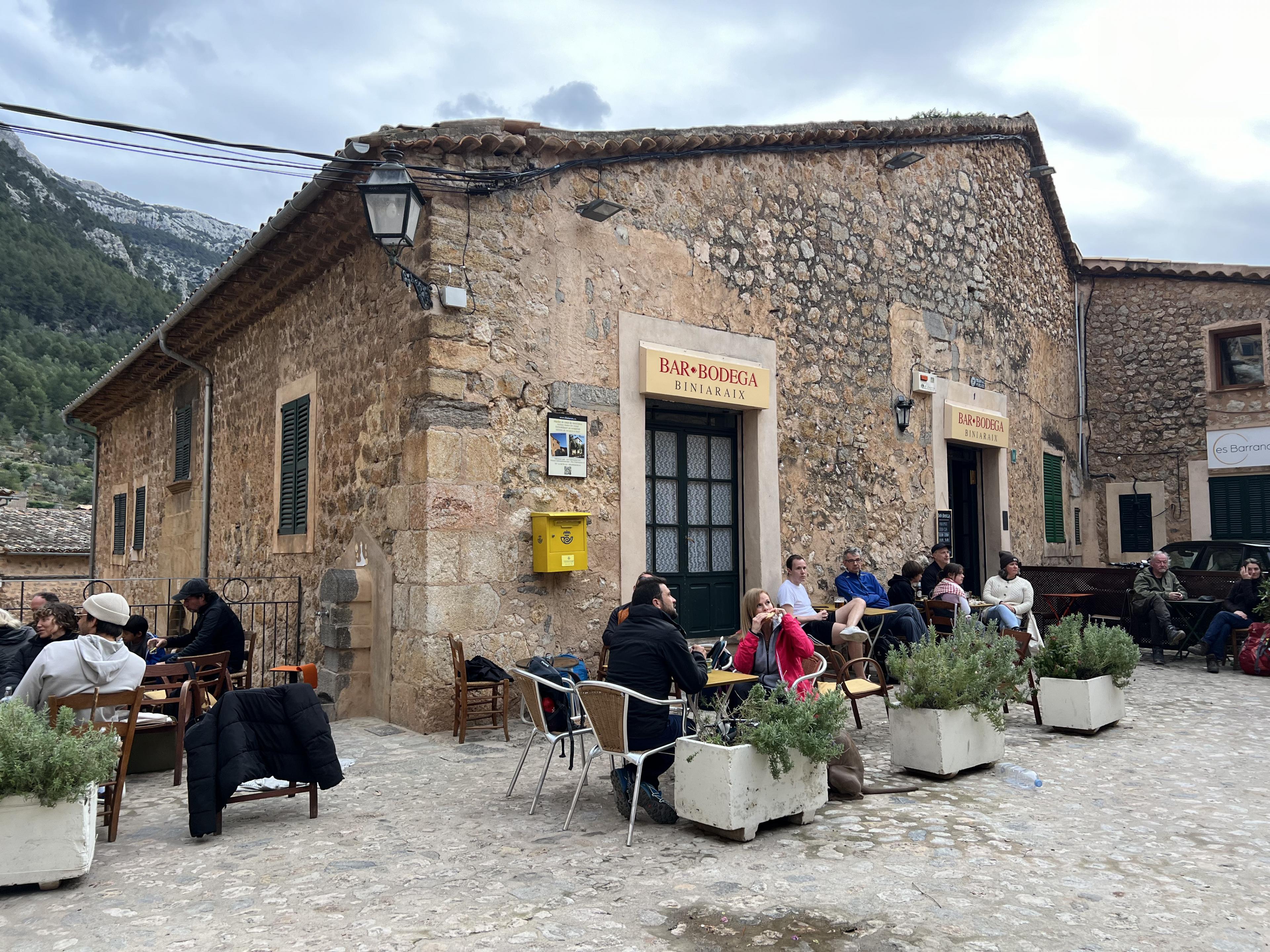 Stone building on a cobbled street surrounded by patrons at tables 
