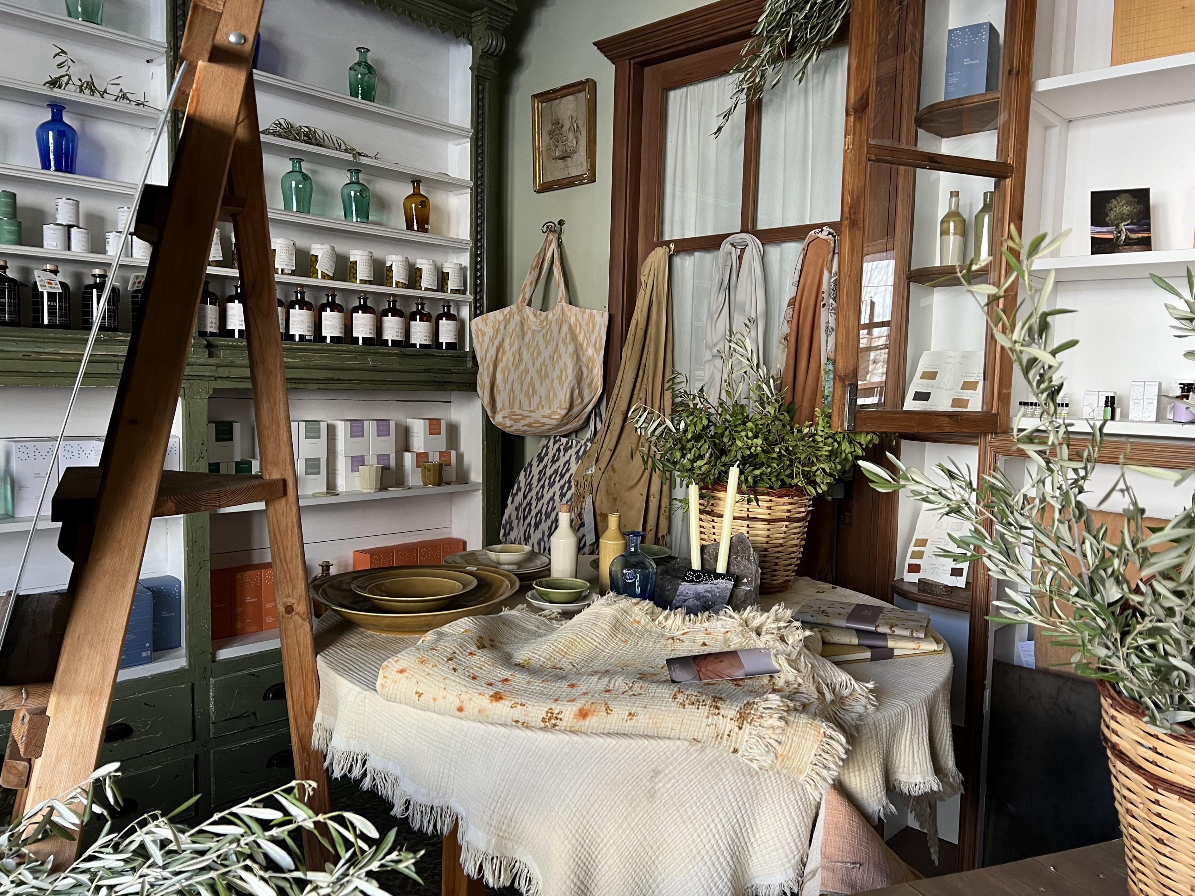 Corner look at the shop with bottles and vases on shelving, a table topped with decor and an easel next to the table 