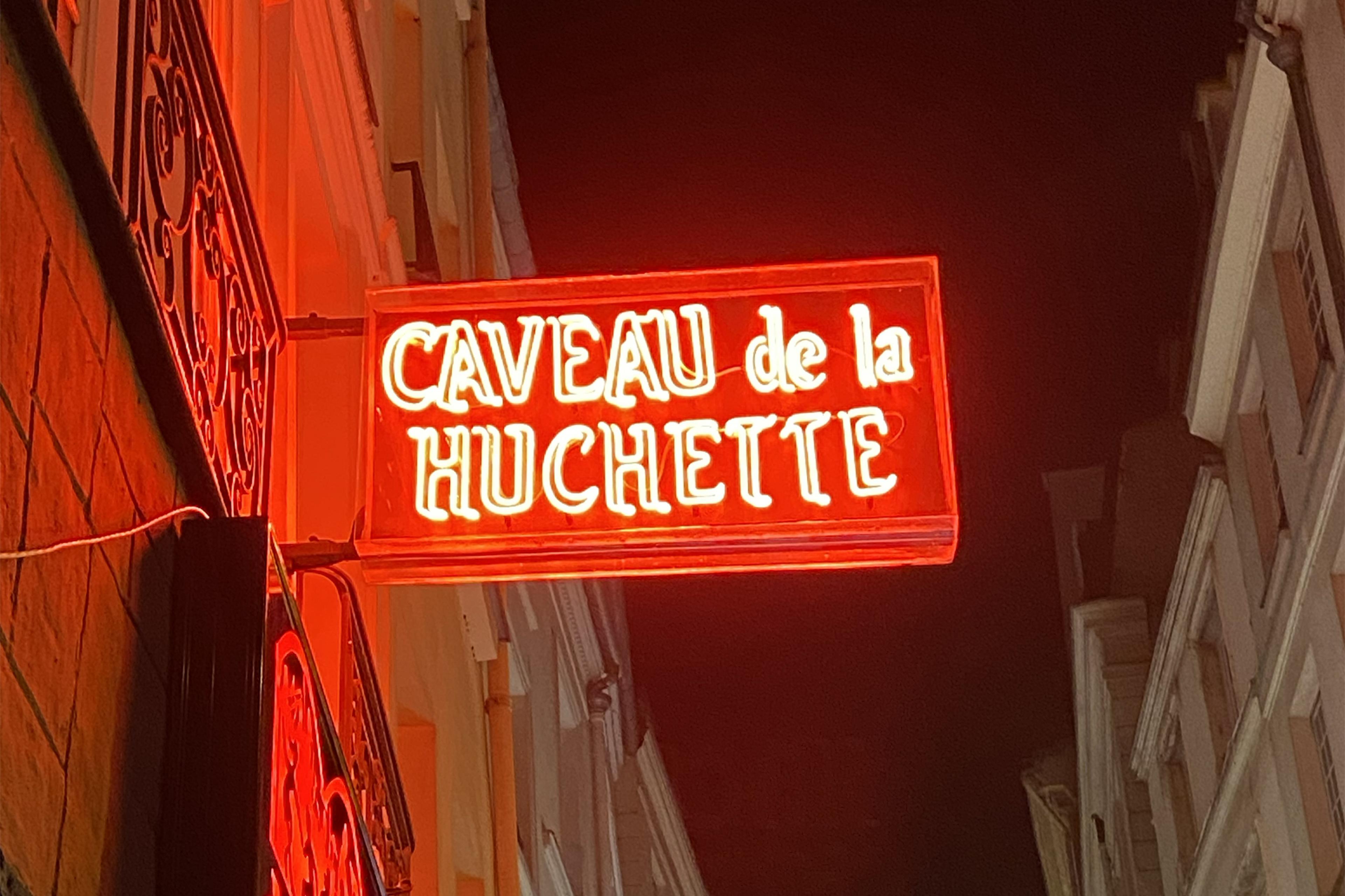 red neon sign sticking out of parisian building saying caveau de la huchette 