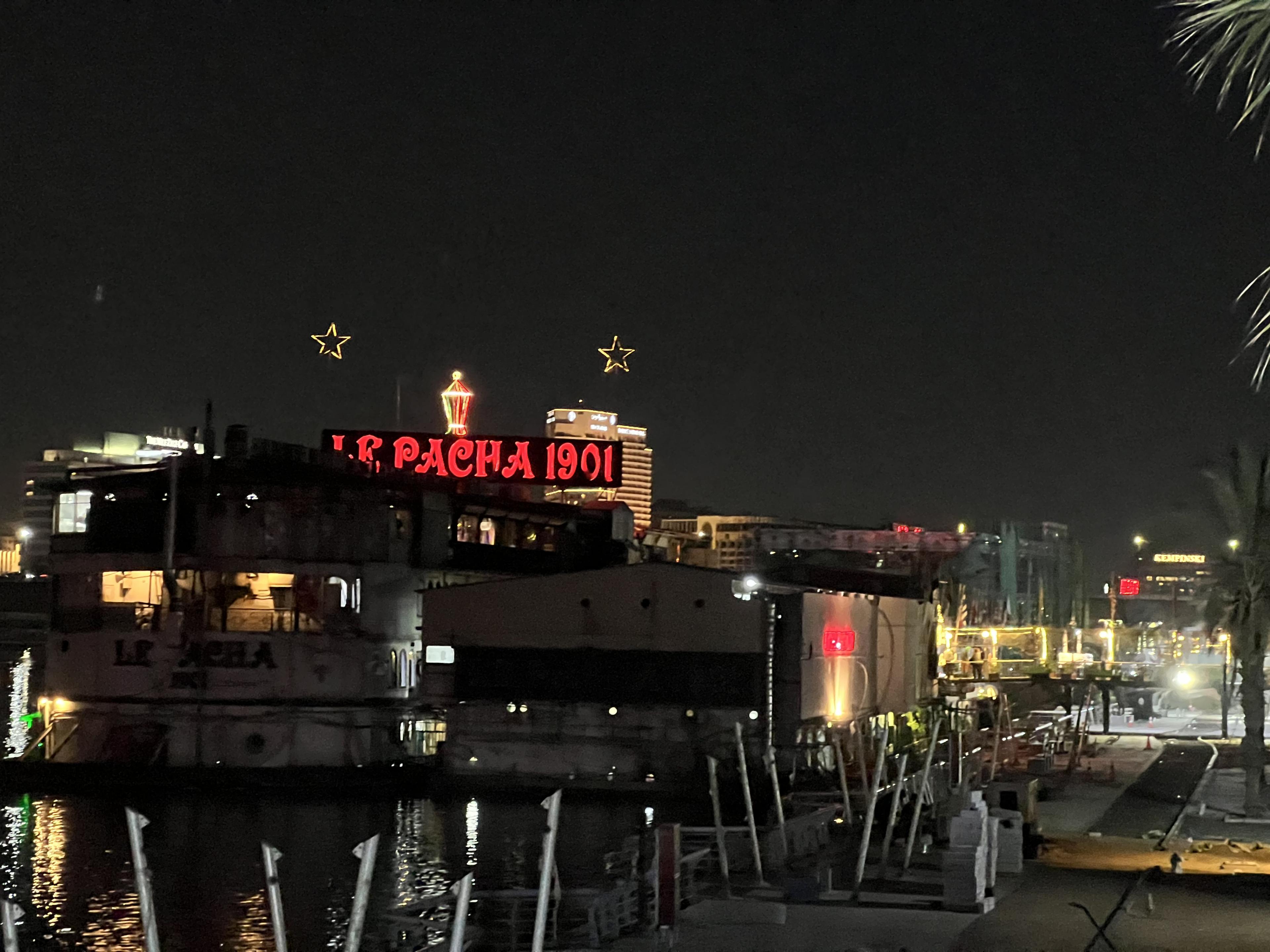 sign at night saying al pacha 1901 in red neon lights above water with boats in front of it