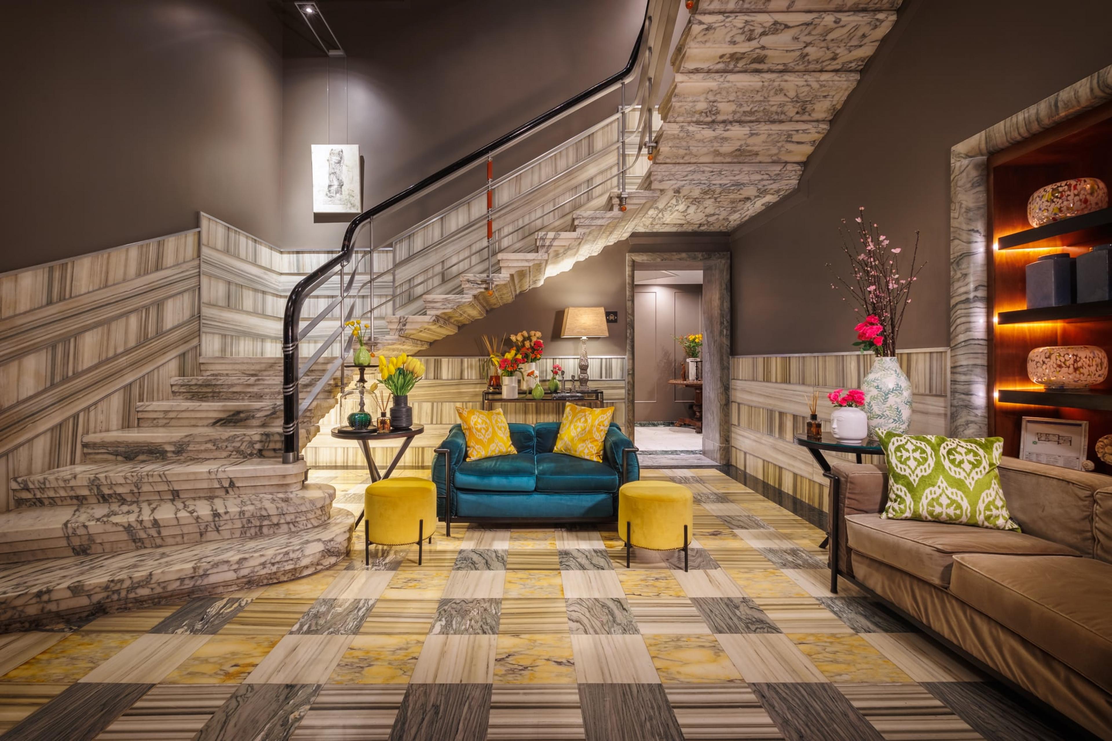 hotel lobby with staircase on left and gray and yellow carpeting with teal sofa at opposite end of lobby