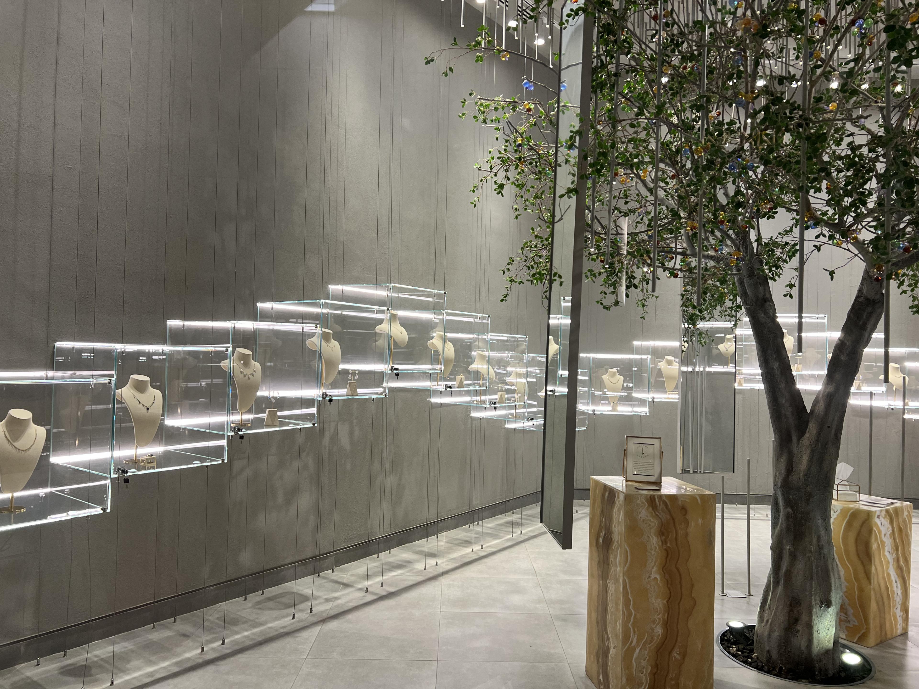 Glass display boxes holding necklaces arranged in a wave-like design against a gray wall 