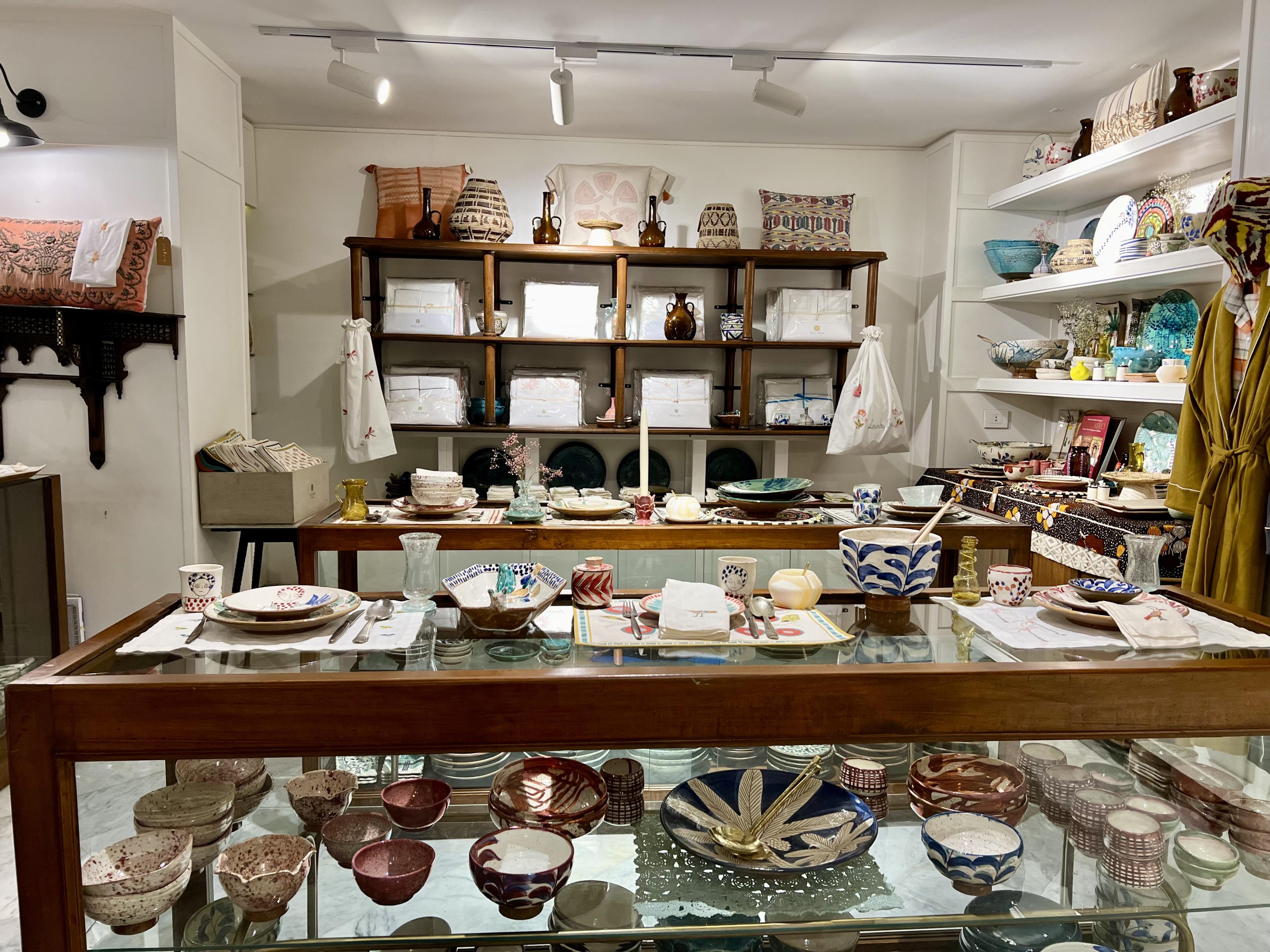 Glass display case full of ceramic bowls and shelving behind stacked with pillows, bowls and vases  