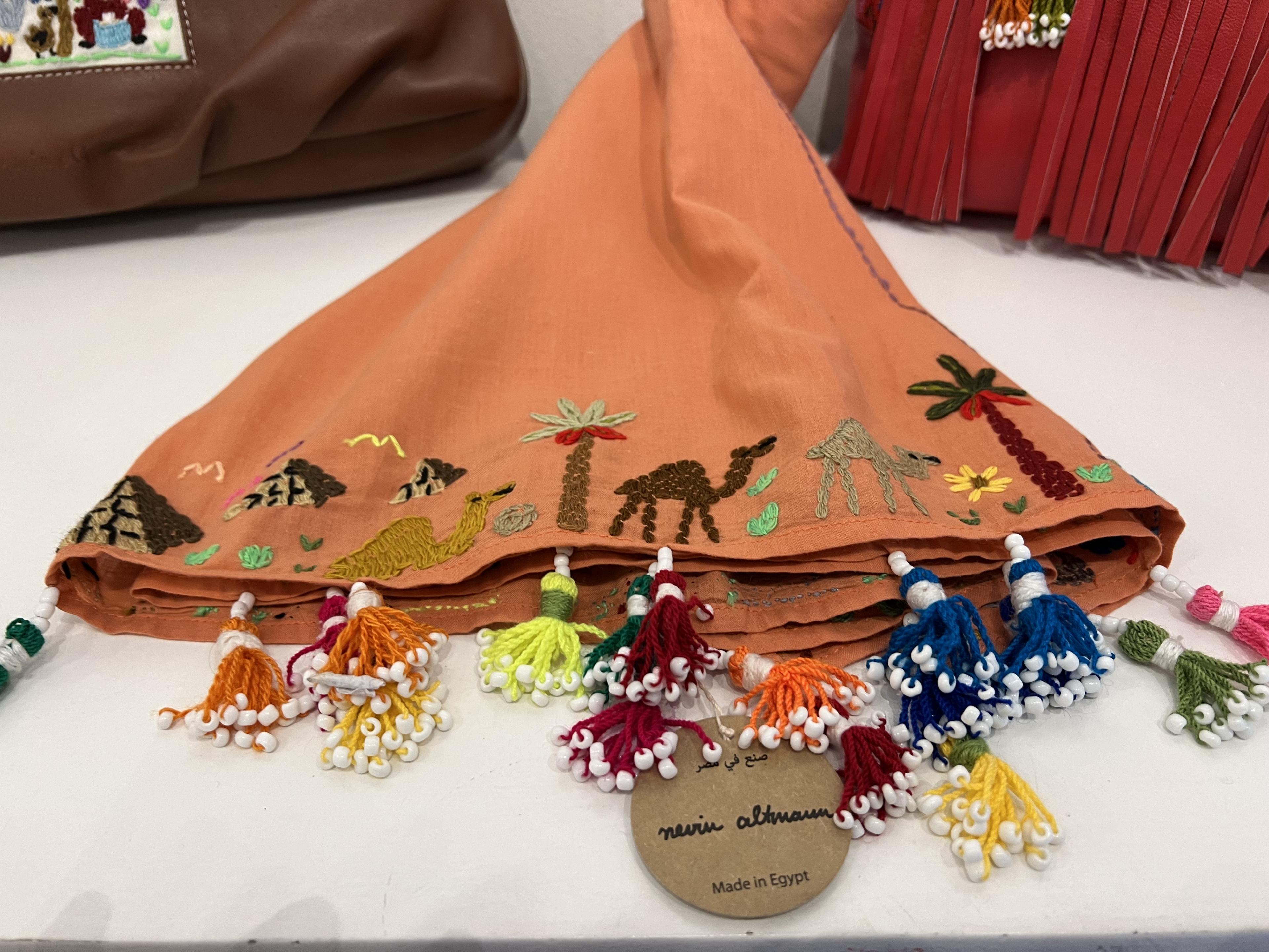 Embroidered orange fabric displaying camels, palm trees and pyramids 