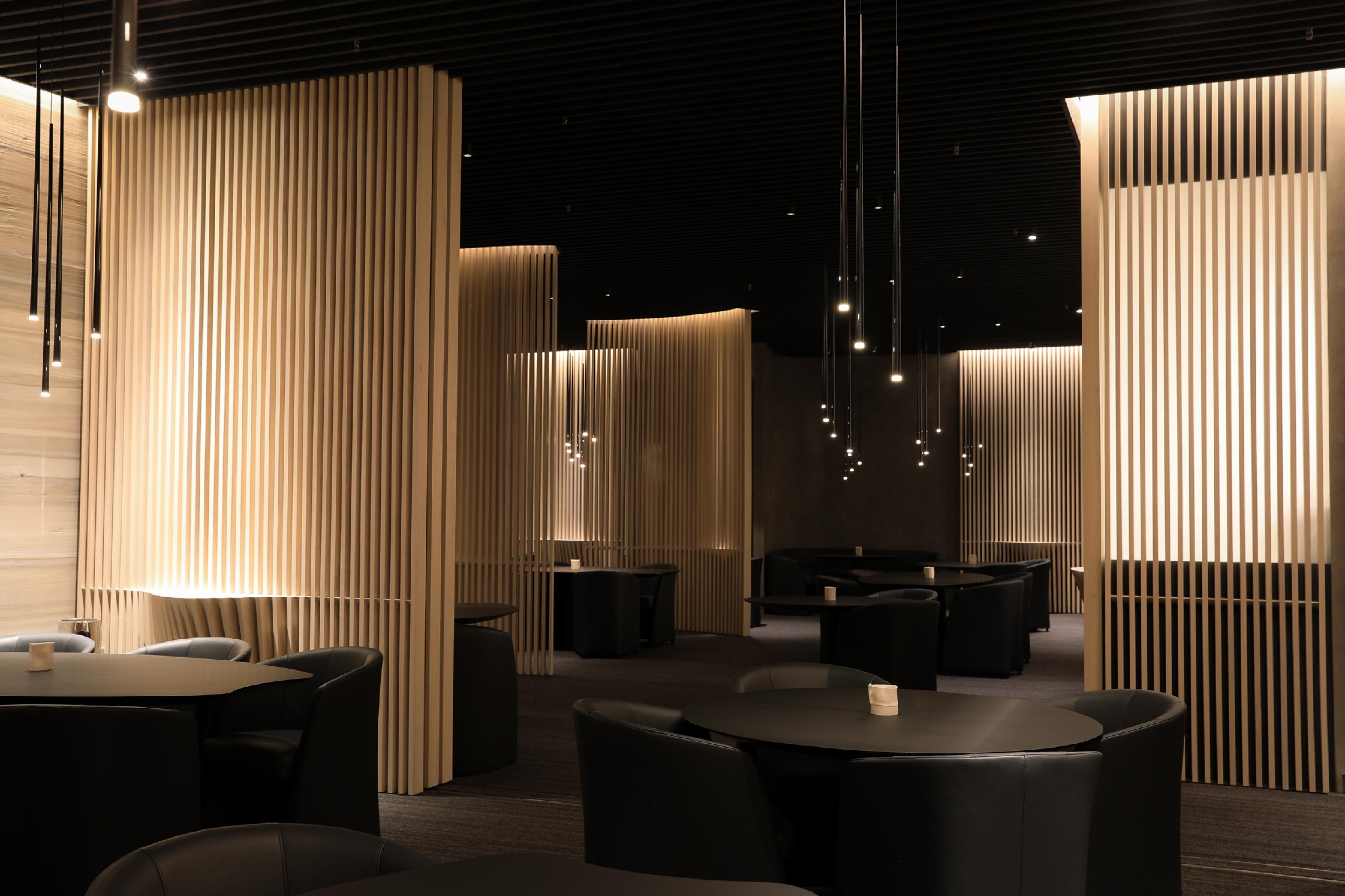 interior of restaurant with dark furniture, lighting and walls and wood sculptures