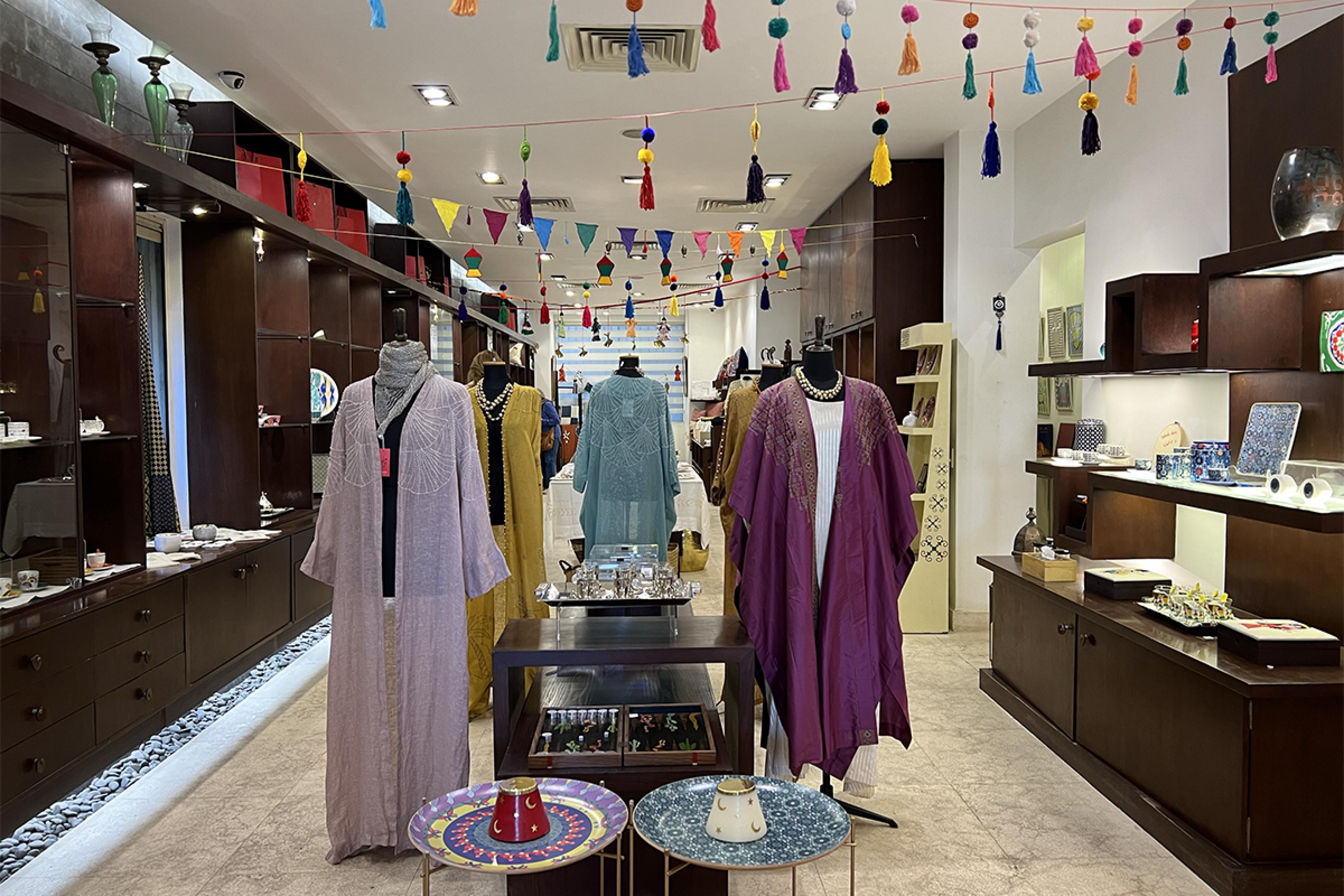 shop with tassels hanging from ceiling and various colorful north african fashions on display in center as well as brown wooden shelves selling small home goods on left and right