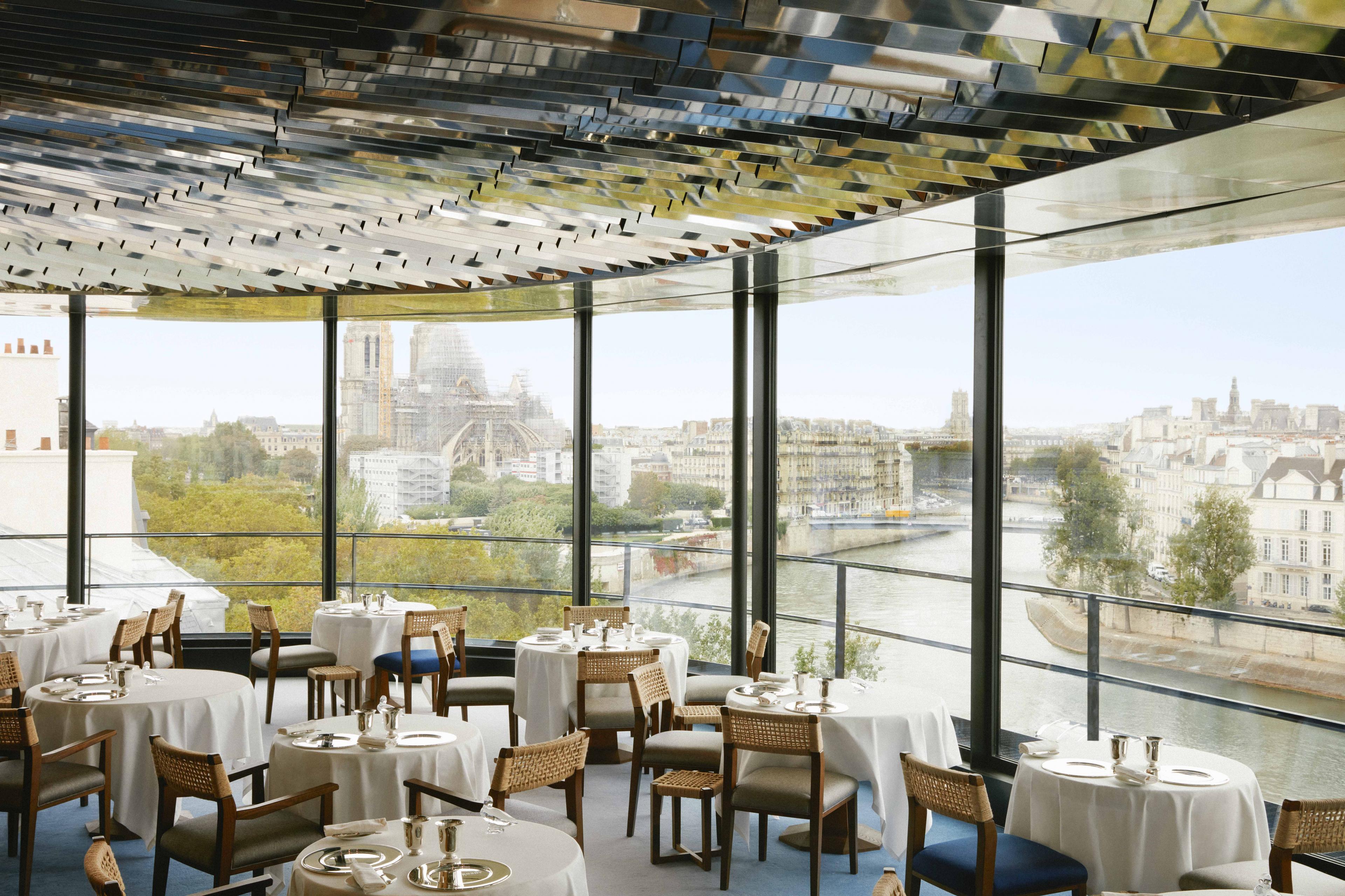 restaurant with floor to ceiling glass windows overlooking a river in a city