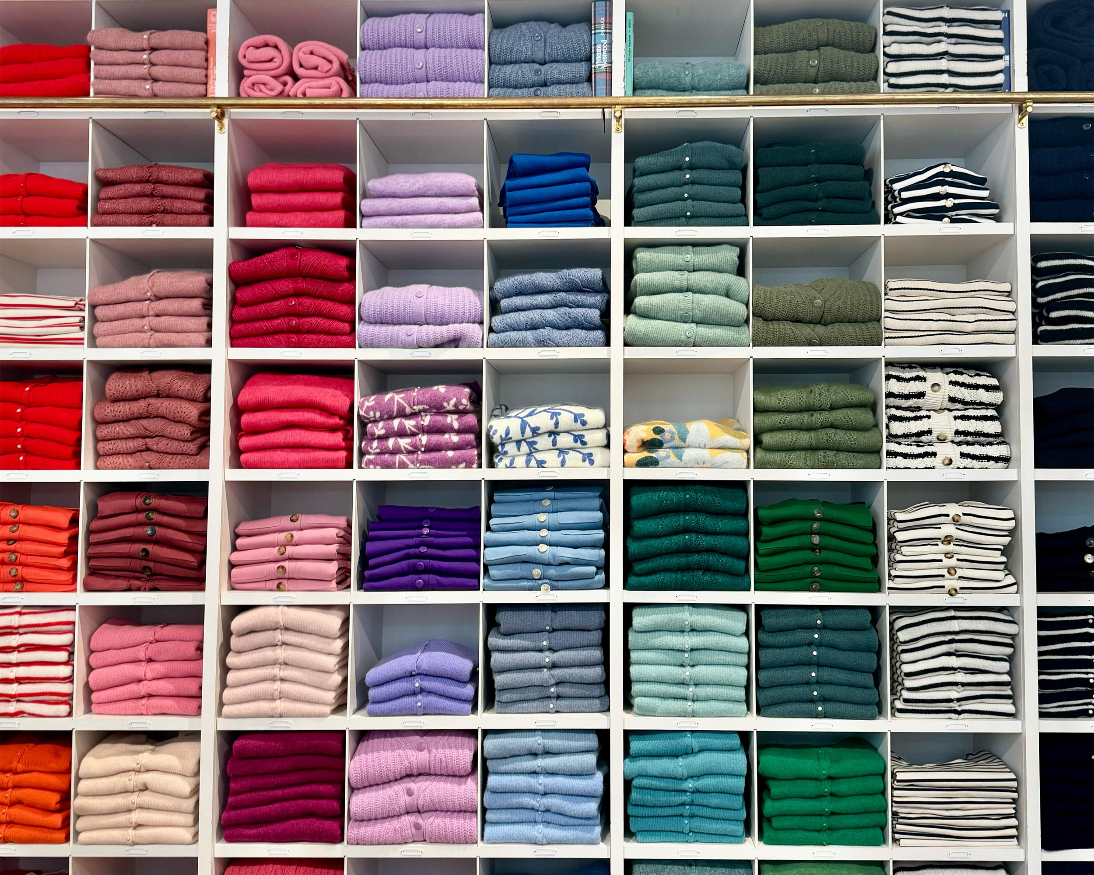 wall of shelves displaying sweaters in many colors folded and arranged vertically sorted by color