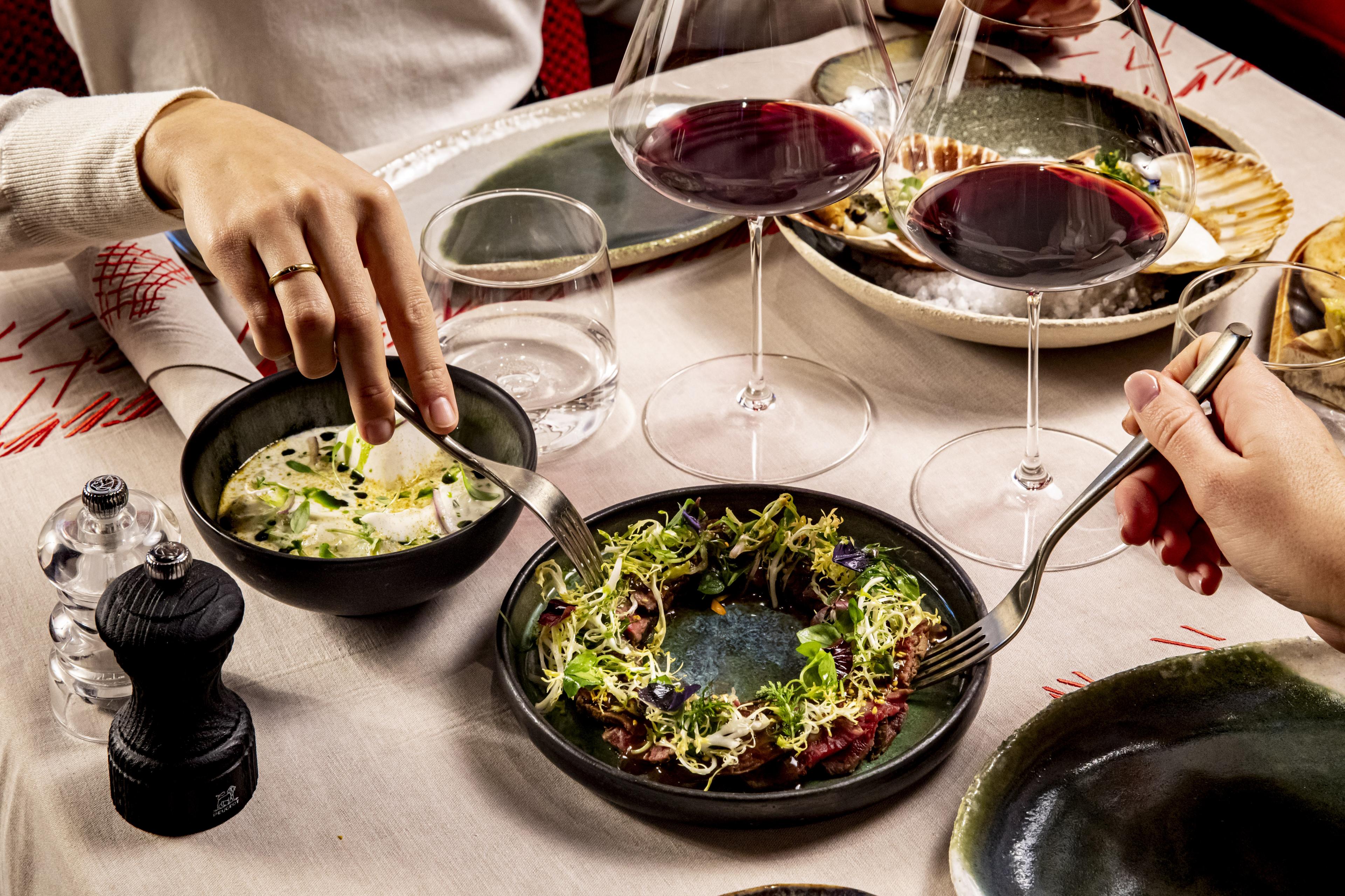 Small table topped with various dishes and two glasses of red wine 