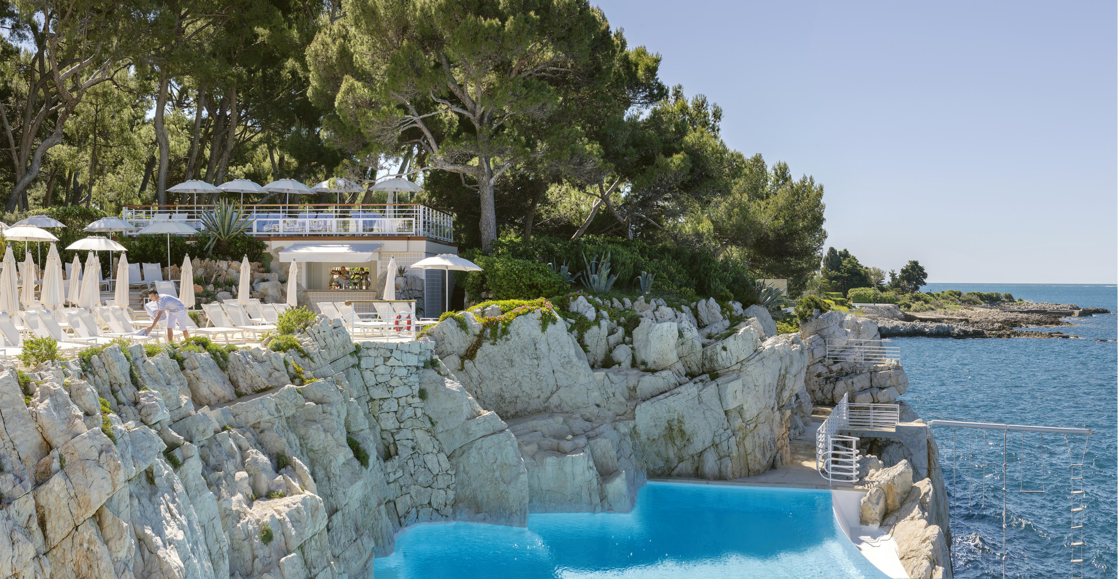 pool built into rocky cliff next to mediterranean with trees on left and sea on right