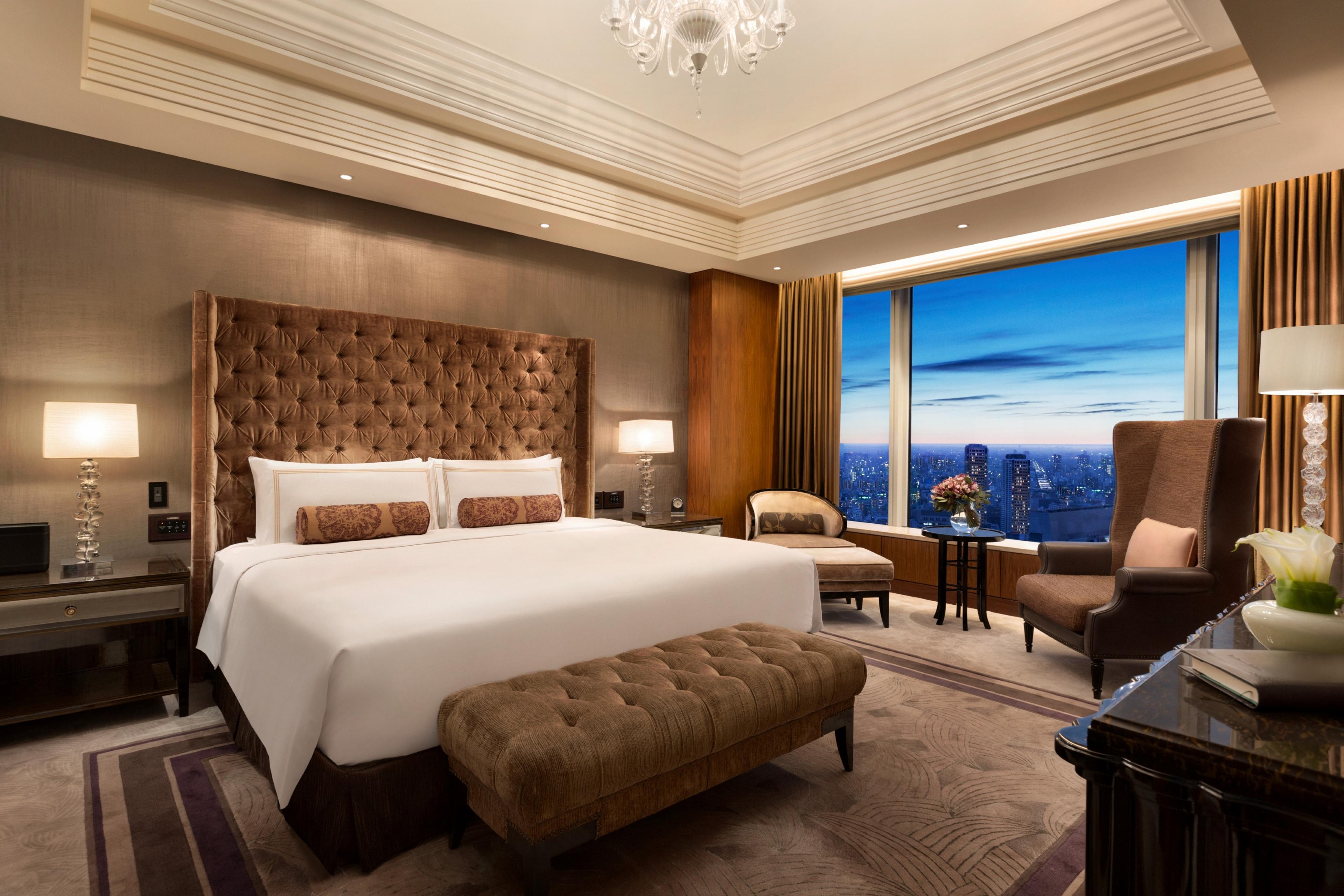 hotel bedroom with a tufted headboard and views of the city at dusk