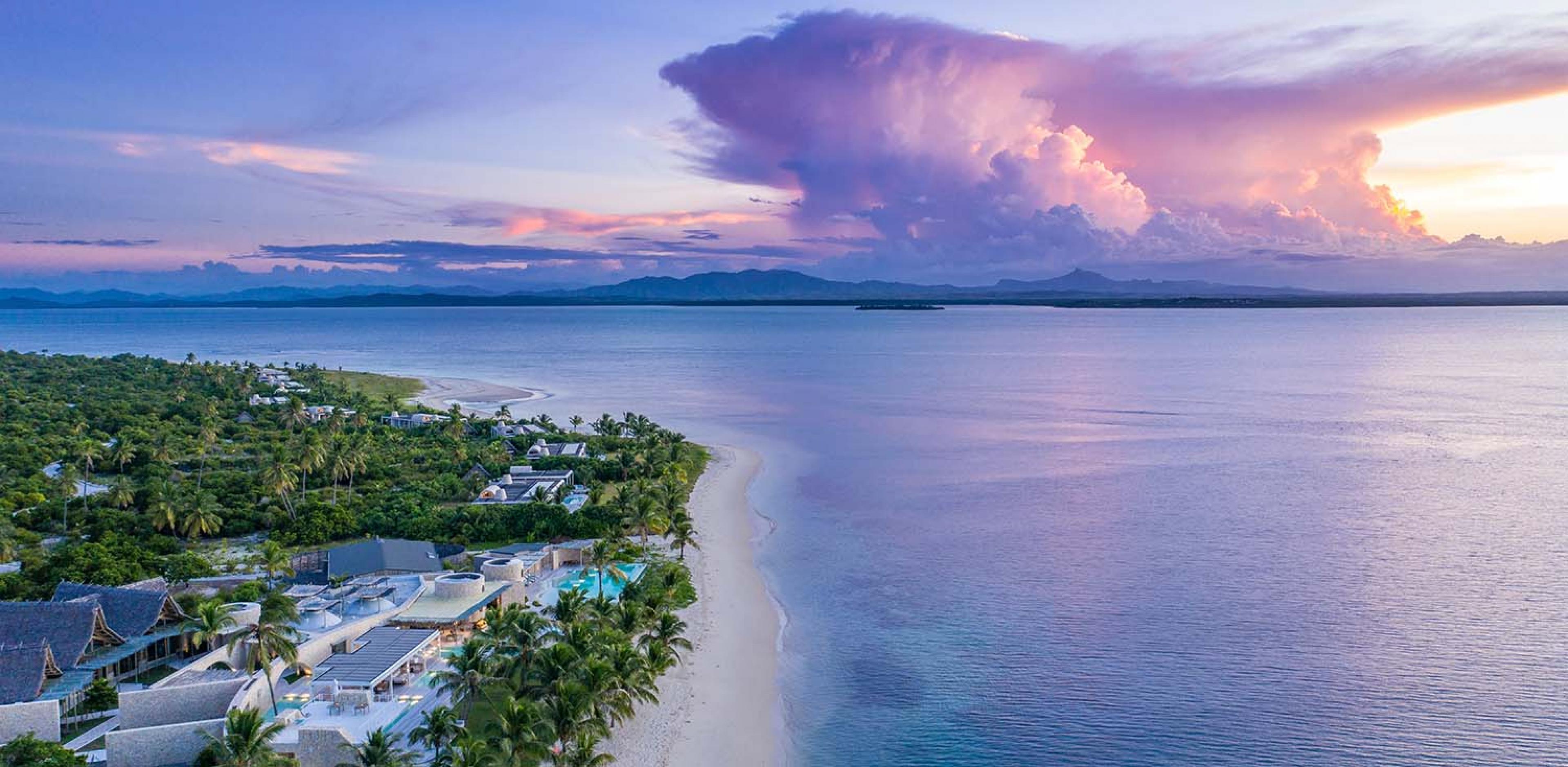 drone view of a villa along the beach and pink and purple clouds reflected in the sea