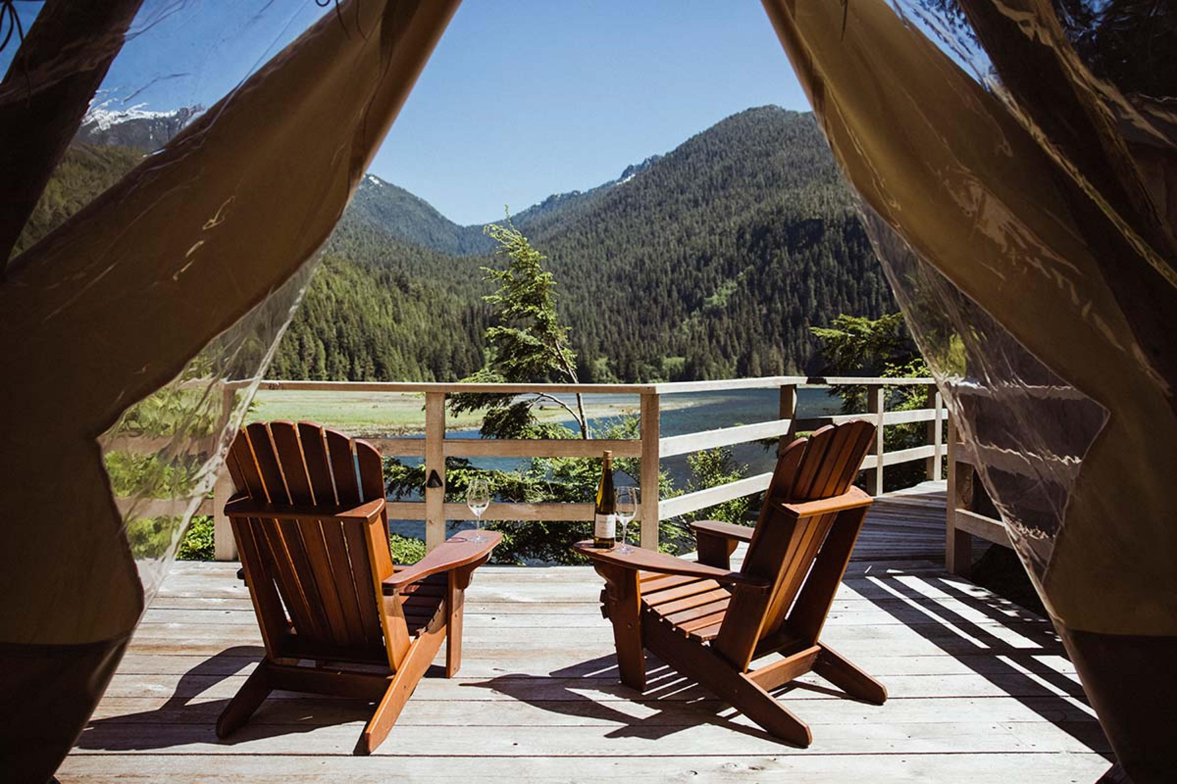 to Adirondack chairs on a wooden deck outside a tent looking out on a lake and mountains