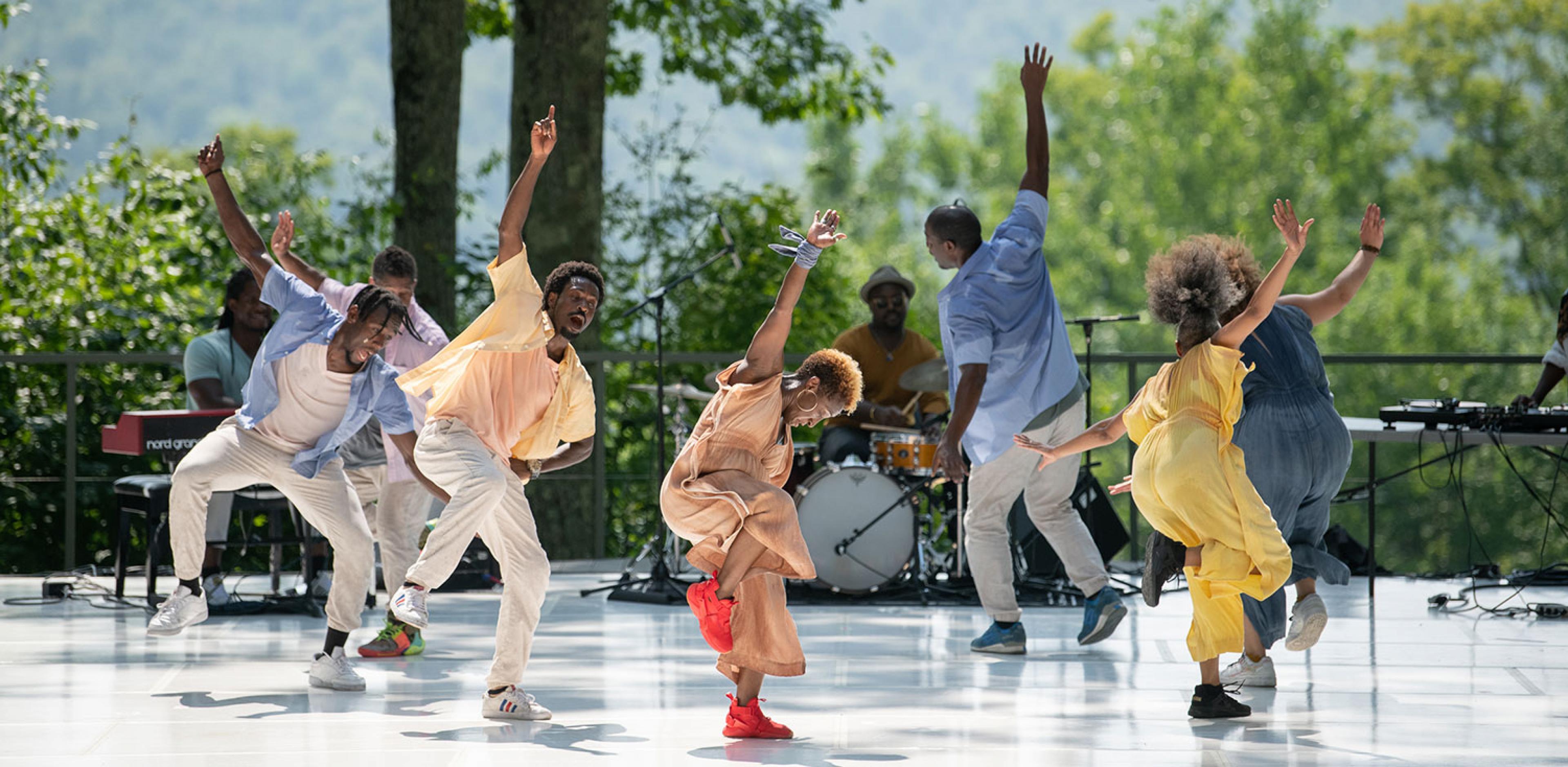 dancers on an outdoor stage with trees in background