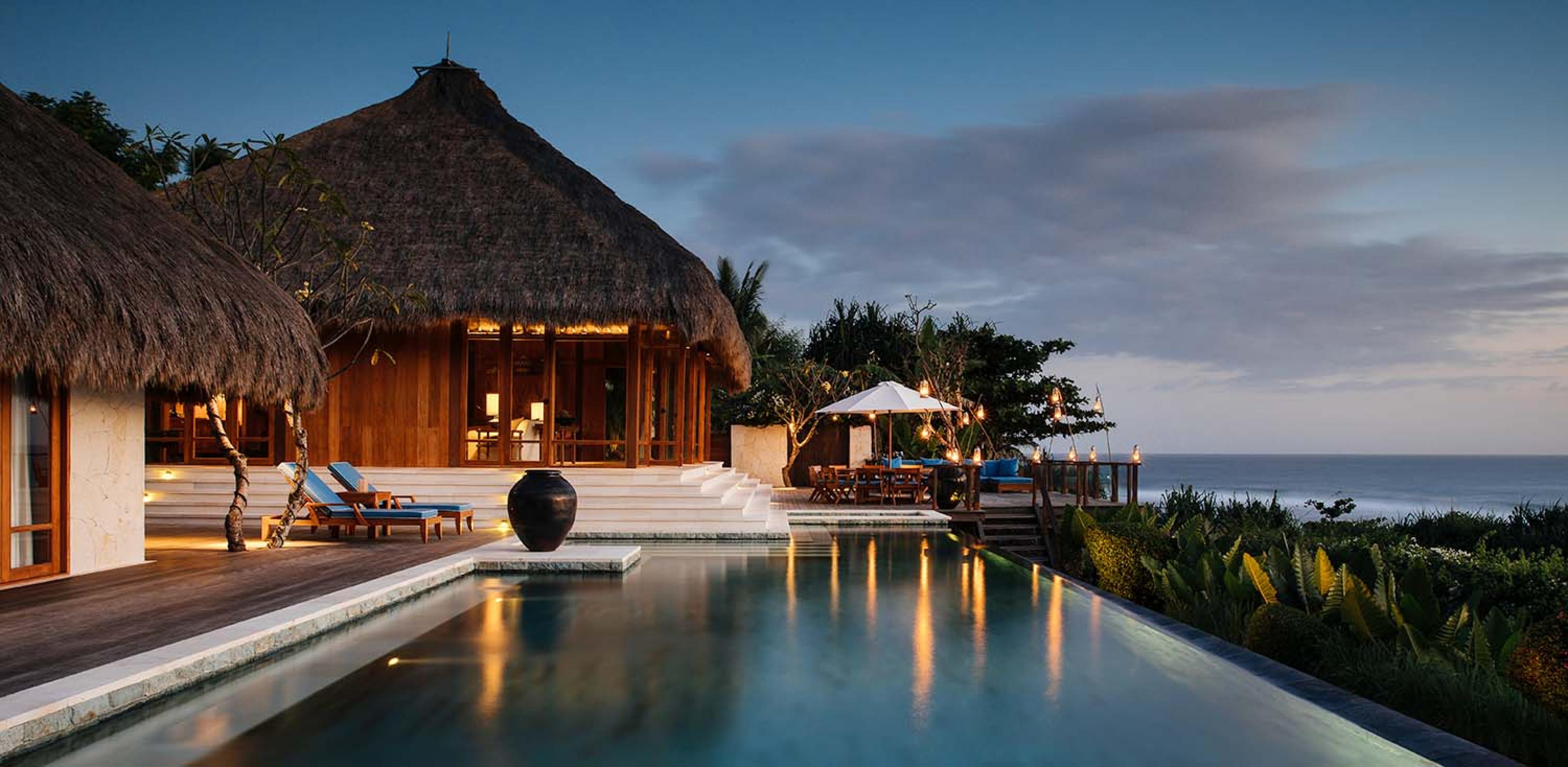 thatched roof villa with white steps leading down to a pool at dusk