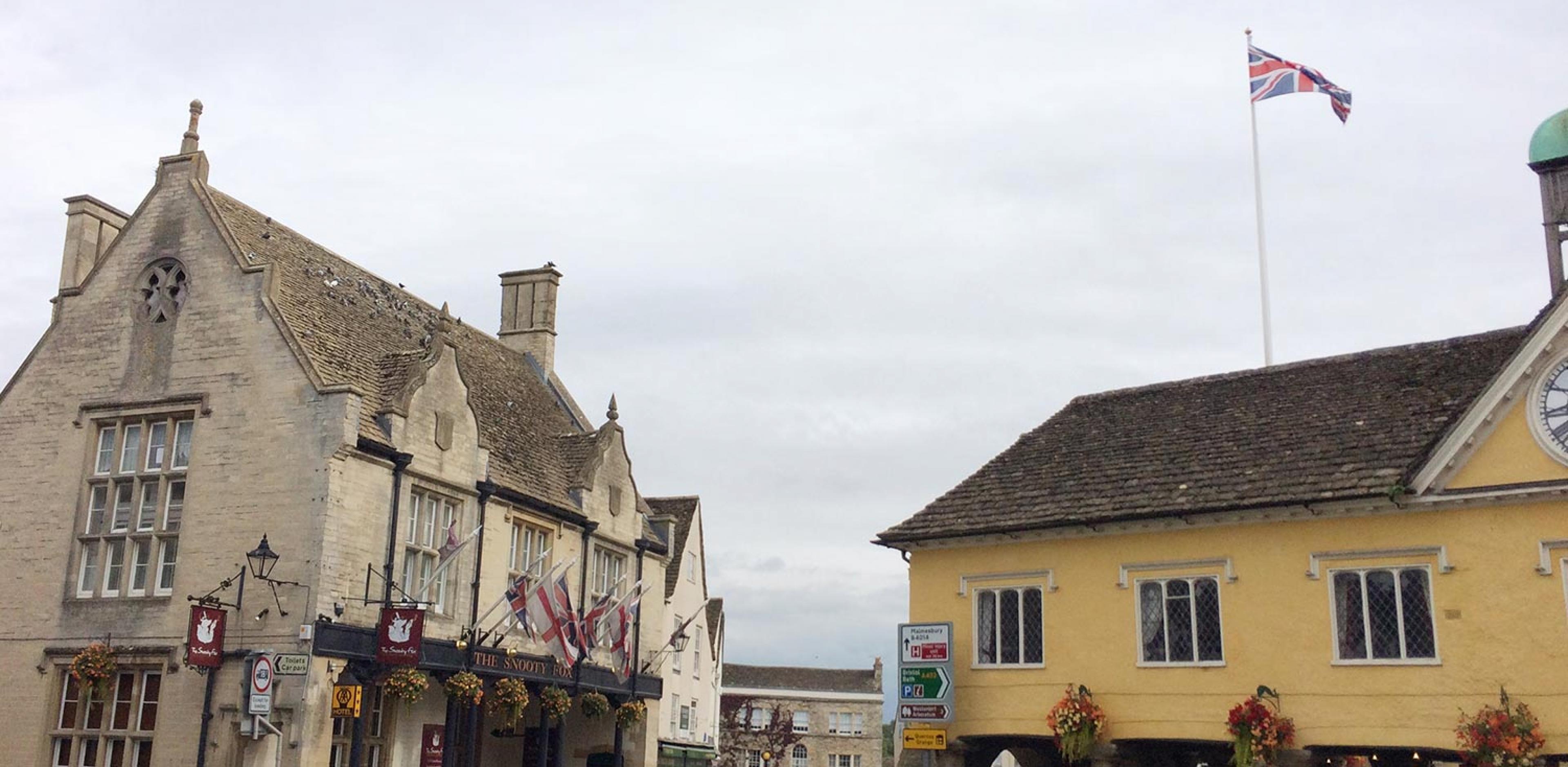 two historic buildings in an english small countrytown's center, one has the british flag flying on a flagpole from the roof 