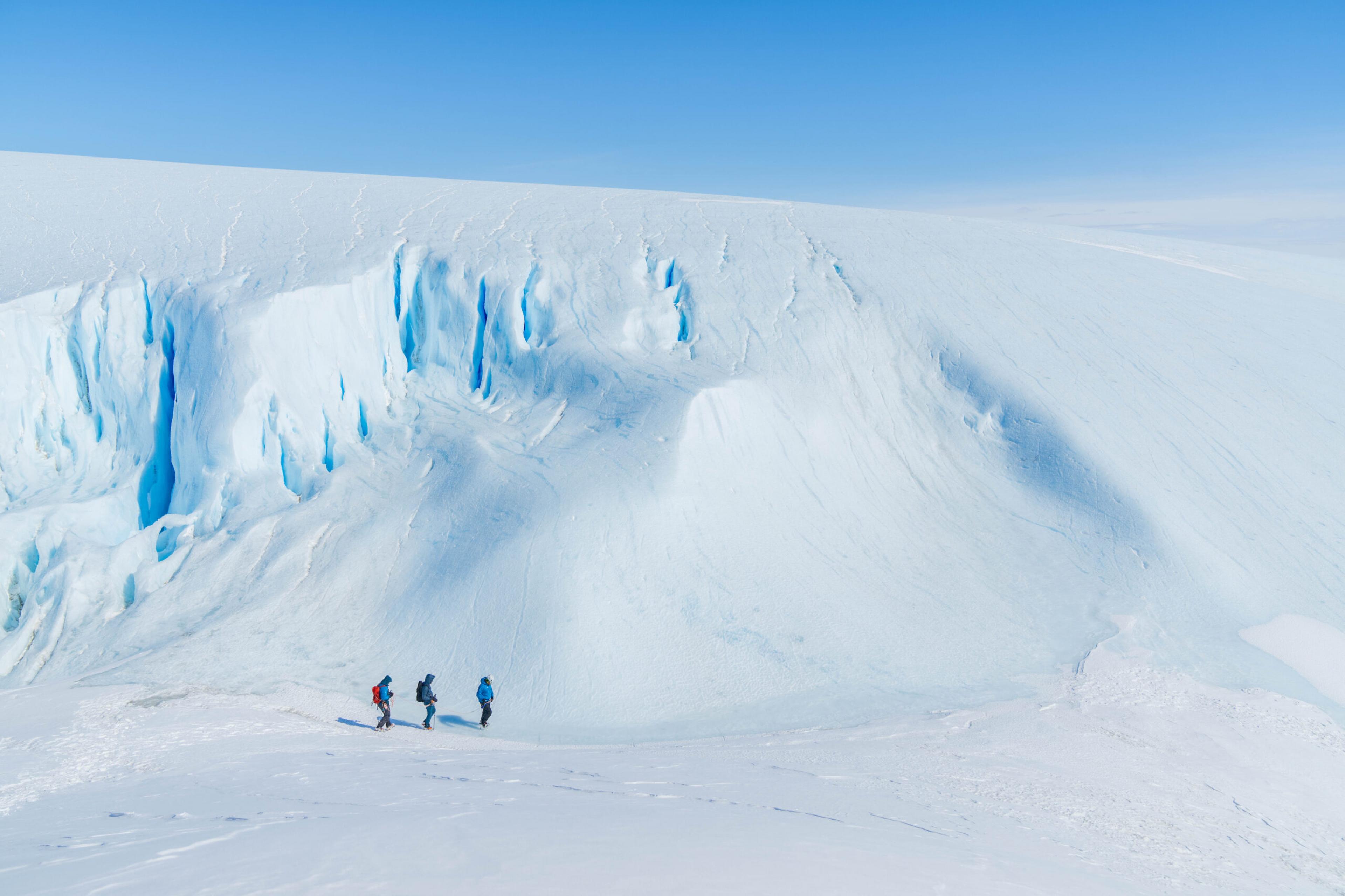 three people hike along a glacier in Antarctica 