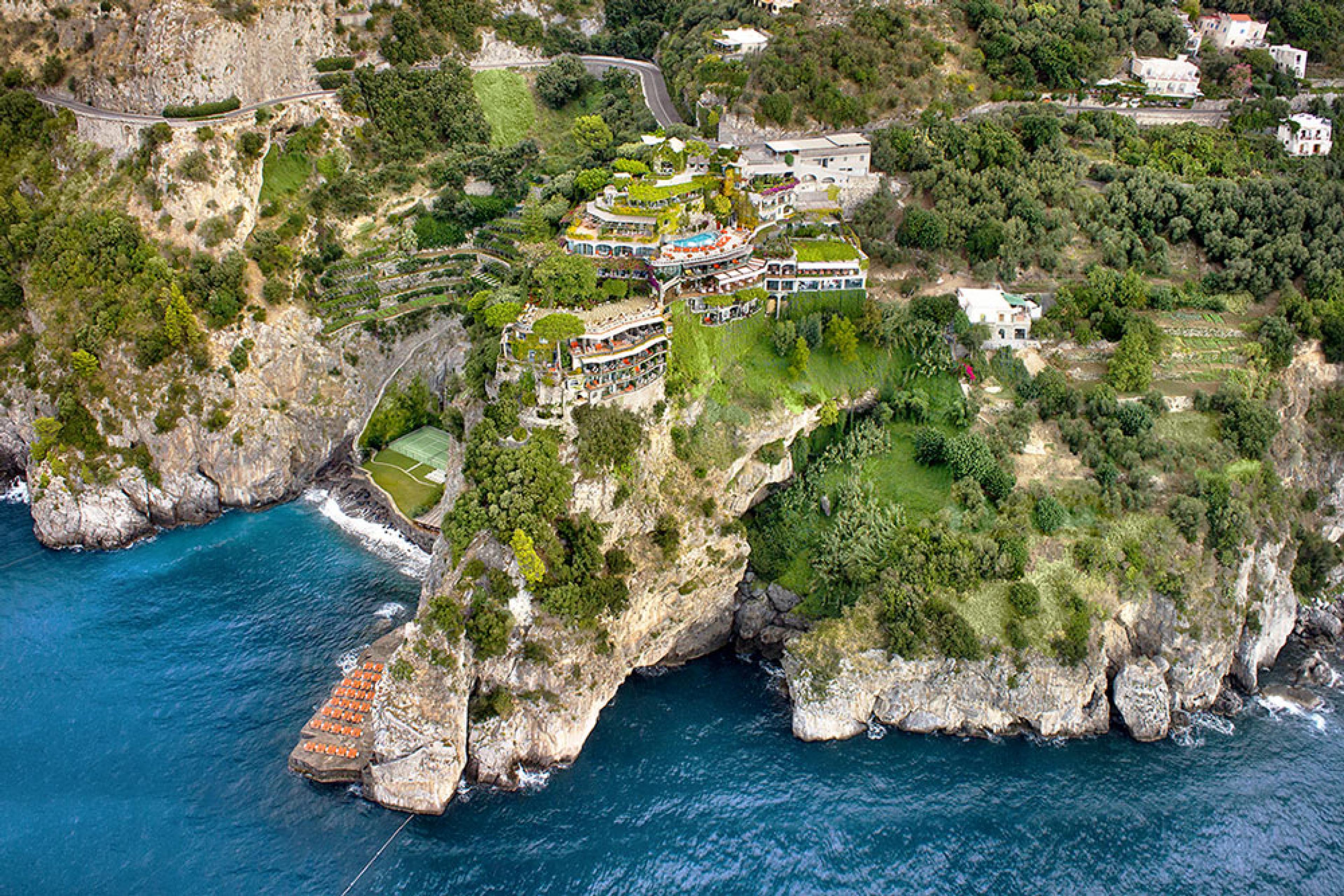 aerial view over a cliffside coastal hotel in italy with green grounds plunging into sea